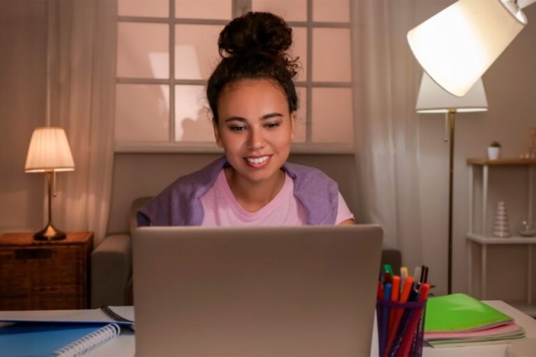 Mujer sonriente trabajando desde casa en su laptop, creando y vendiendo productos digitales rentables.